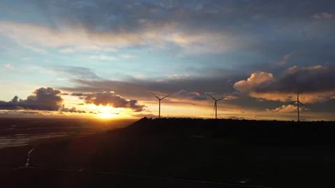 Slow Drone Pulling Away from Wind Turbines on Hill at Sunset Silhouette Stock Footage 325796981