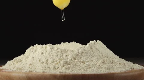 SLOW: Egg falls on a pile of flour on a black background Stock Footage 62827906