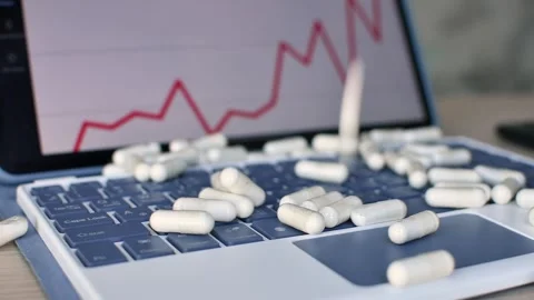 Slow falling capsules hit laptop keys as red medical chart shows digital Stock Footage 336623682