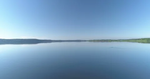 Slow flight over the surface of wide lake with calm water and clear blue sky Video stock 111959570