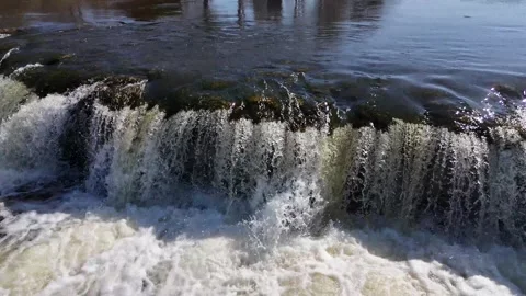A slow flight past a gently flowing waterfall, sunlight glinting on the river Stock Footage 307494764