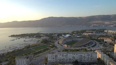 Slow fly in the evening over buildings with Split stadium in the background Stock Footage 96137097