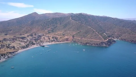 Slow forward aerial shot approaching harbor town with a sandy beach and hills. Video stock 88673039