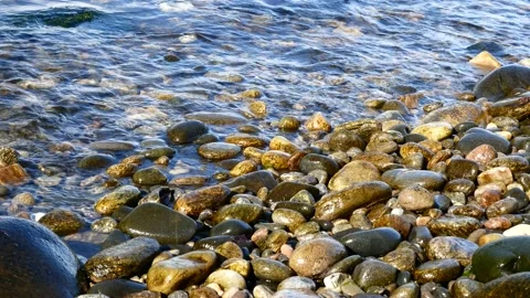 Slow, gentle waves breaking on a clean pebble beach on a sunny day Stock Footage 140512354