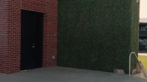 Slow left to right pan from brick wall and hedge to baseball stadium field Stock Footage 332633198