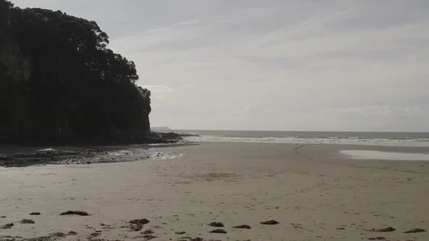 Slow &amp; low aerial push out over sandy beach towards calm waves and rocks 4K HDR Stock Footage 113898515