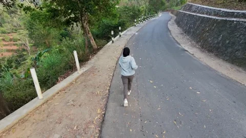 Slow mo back view of hijab woman jogging on empty rural road. Видео 342334859