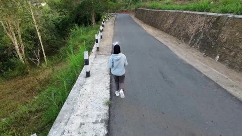 Slow mo back view of hijab woman jogging on empty rural road. Stock Footage 342334913