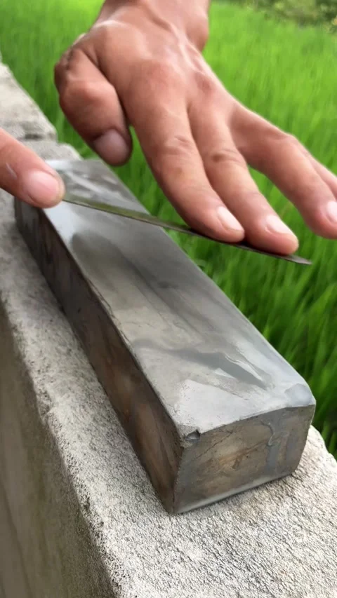 Slow mo close up hands sharpening sickle on whetstone by green rice field. 스톡 동영상 342516266
