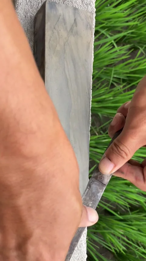 Slow mo close up hands sharpening sickle on whetstone by green rice field. Stock Footage 342516267