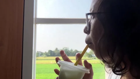 Slow mo close up woman drinking green iced drink by window with rural rice field Stock Footage 342334744