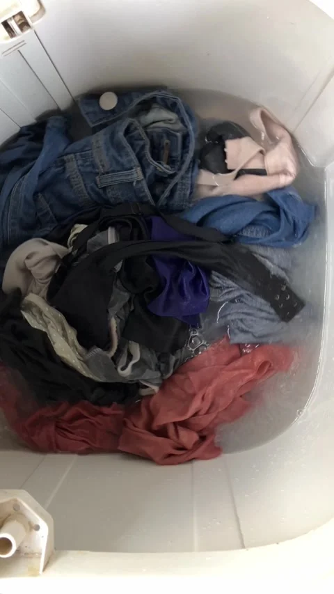 Slow mo dirty clothes soaking and spinning inside top load washing machine. Stock Footage 343099152