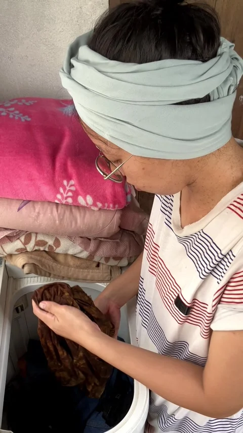 Slow mo high angle woman putting clothes into top load washing machine. Stock Footage 343099410