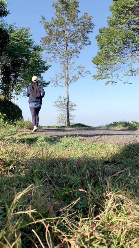 Slow mo low angle of hijabi woman jogging on rural asphalt road in nature. Stock Footage 341314811