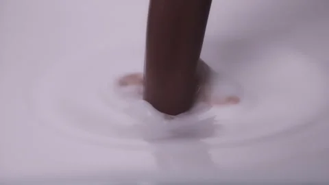 Slow mo, macro shot: Melted chocolate pouring into milk. UHD25p Stock Footage 249590475