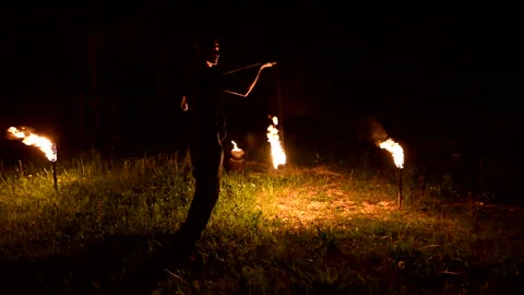 Slow-mo of man in dark rotates burning ball poi. Low key. Fire show. Close-up. Stock Footage 123997225