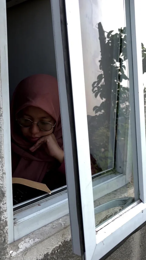 Slow mo outside view muslim woman in hijab reading book by open window. Vídeo Stock 343098743