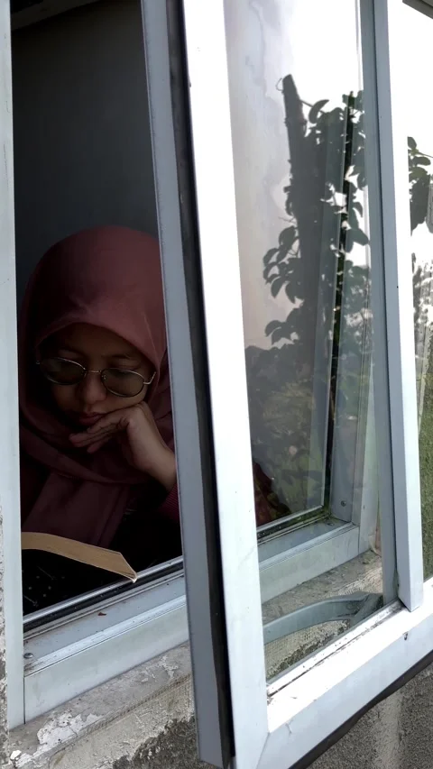 Slow mo outside view muslim woman in hijab reading book by open window. Stock Footage 344996277