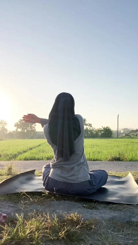 Slow mo rear view of hijabi woman doing arm stretch on yoga mat by rice field Vídeo Stock 340447800
