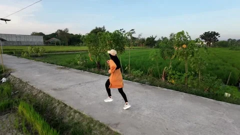 Slow mo side view of hijabi woman jogging on rural road by rice field. 動画素材 341835274