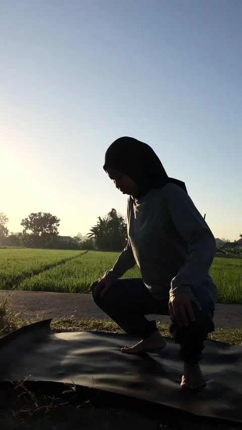 Slow mo silhouette of hijabi doing malasana yoga by a rice field at sunrise Stock Footage 340447612