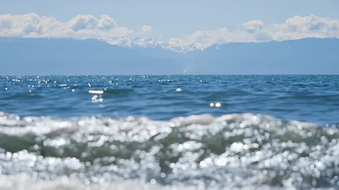 Slow mo small waves rolling onto beach with huge mountains in distance	 Vídeo Stock 122232334