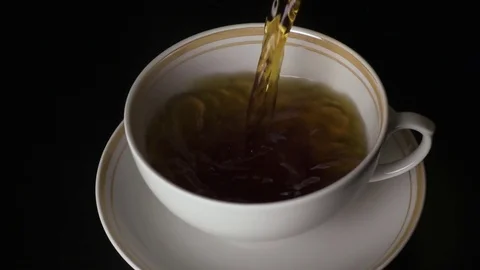 Slow mo. The tea is poured into a cup and saucer on a black background Stock Footage 74267835