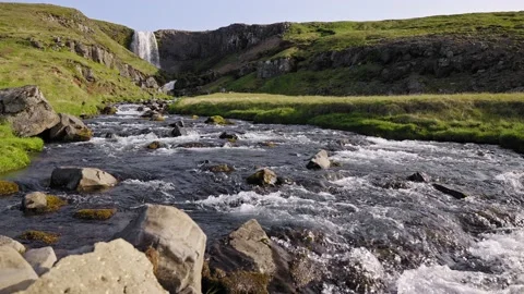 Slow-mo view of waterfall over unique rock formations with lush green grass Video stock 160784514