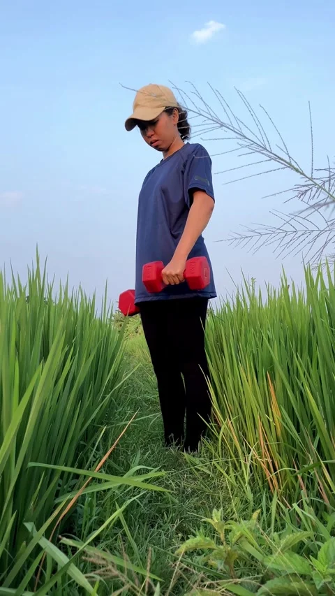 Slow mo woman with cap doing dumbbell bicep curl in tall green grass. 스톡 동영상 342369206