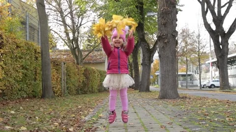 Slow motion, a 4-5-year-old girl throws up maple yellow leaves on a neutral urba Stock Footage 227514582