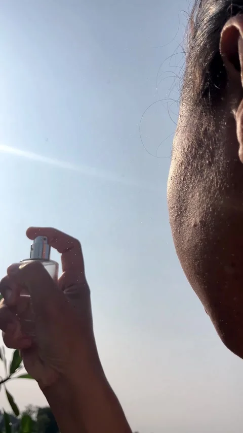 Slow Motion 4K Over the Shoulder of Young Woman Spraying Face Mist Summer Stockbeeldmateriaal 337641896