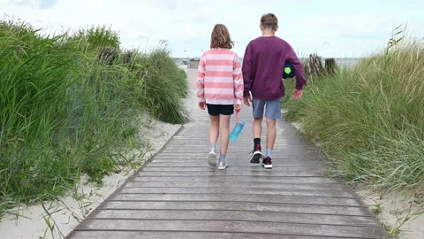 Slow motion 4K video of walking children on wooden pathway at white beach in Stock Footage 201825297