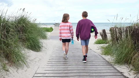 Slow motion 4K video of walking children on wooden pathway at white beach in Stock Footage 201825982