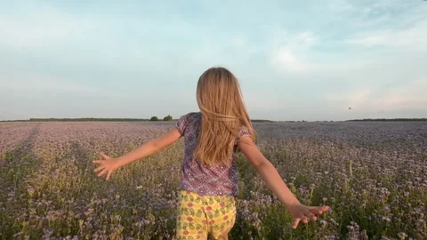 Slow motion of a 6-10 year old blonde girl running across a summer field with 스톡 동영상 134637607