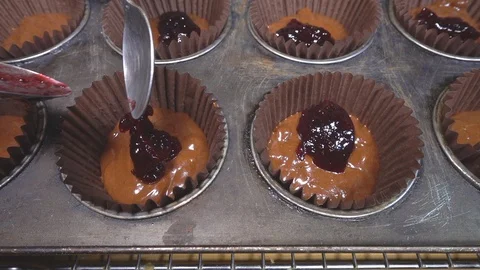 Slow motion - Adding jam to wet muffin mix in paper cases in a baking tray. 스톡 동영상 99778717