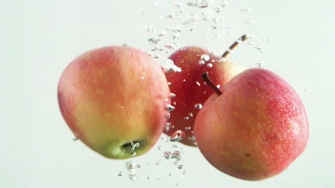 Slow motion of  apples falling into clear water with white background. Stock Footage 241324299