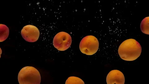 Slow motion apricots falling into transparent water on black background Stock Footage 246044617