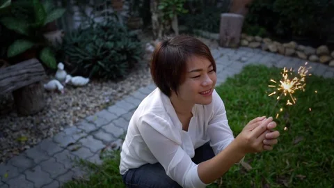 Slow motion Asian woman sit and play sparking stick in a garden Stock Footage 87737853