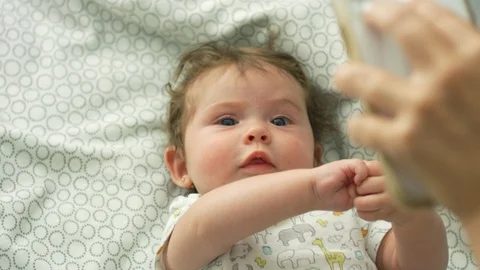 Slow motion of baby looking up at cell phone while lying down in bed Stock-Footage 114644875