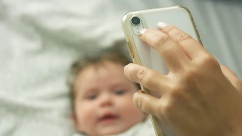 Slow motion of baby lying in bed and smiling at cell phone Stock Footage 114645206