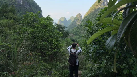 Slow motion back view of male tourist with backpack taking photo of scenic karst 스톡 동영상 336466454