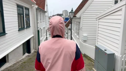 Slow motion back view of a young woman in a hooded raincoat walking alone Video stock 331872221