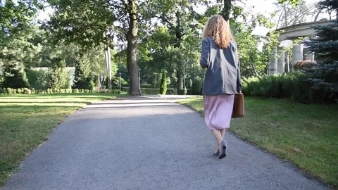Slow motion back view of a young blonde woman walking through a park. 库存影片 333058670