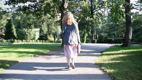 Slow motion back view of a young blonde woman walking through a park. Vídeo Stock 333058690