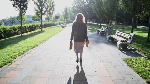 Slow motion back view of a young blonde woman walking through a park. Vídeo Stock 333070241