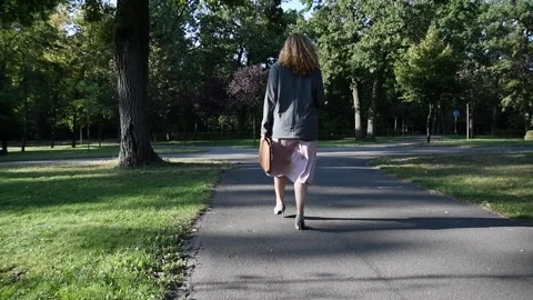 Slow motion back view of a young blonde woman walking through a park. Vídeo Stock 333070247