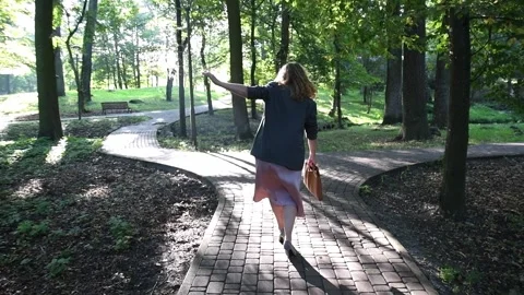 Slow motion back view of a young blonde woman walking through a park. Vídeo Stock 333070288