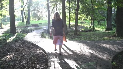 Slow motion back view of a young blonde woman walking through a park. Vídeos de archivo 333070341