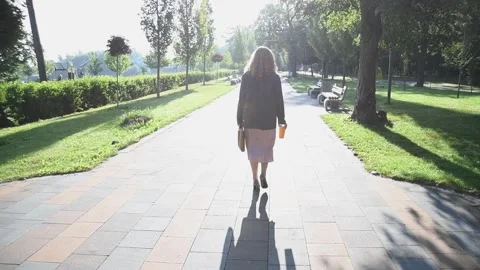 Slow motion back view of a young blonde woman walking through a park. Vídeos de archivo 333070346