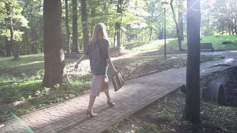 Slow motion back view of a young blonde woman walking through a park. Vídeos de archivo 333070388
